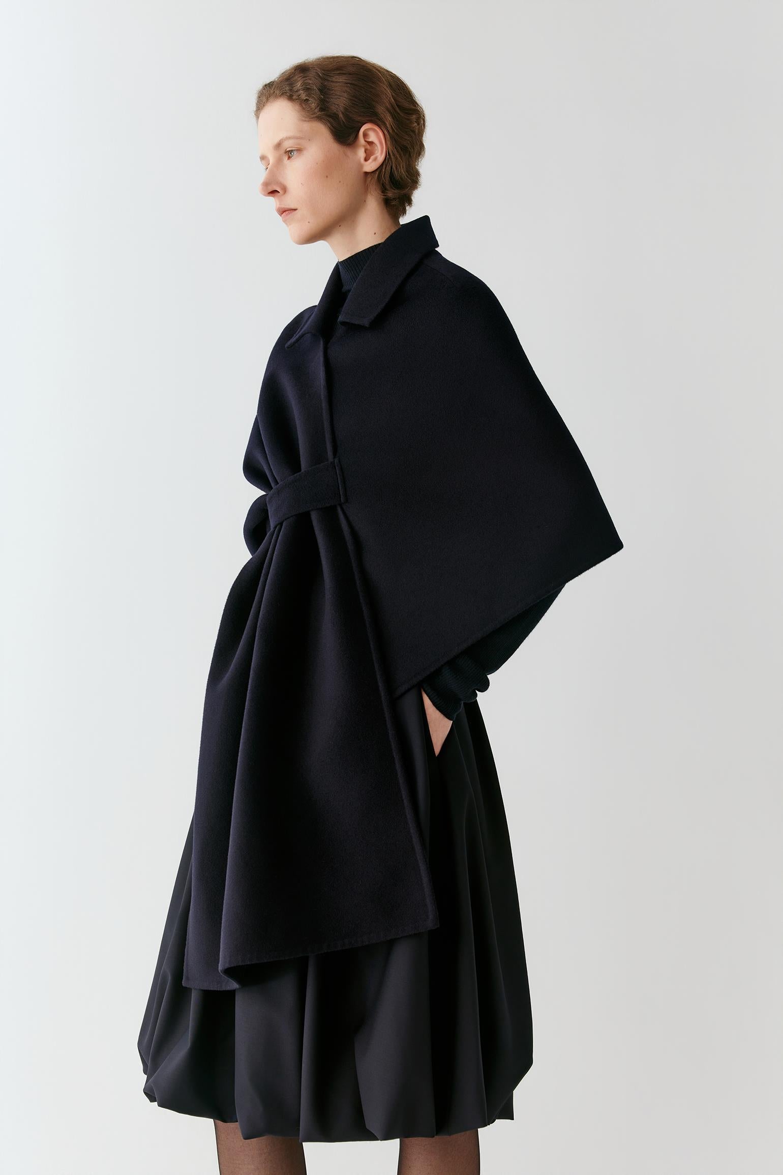 Video of a woman wearing a deep black wool and silk cape, showing the movement of the asymmetric silhouette and fluid drape as she moves.