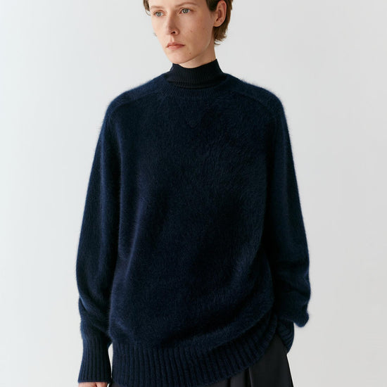 Video of a woman wearing a blue-black cashmere pullover, showing the relaxed silhouette, ribbed mock neck and natural movement of the softly structured knit as she moves.