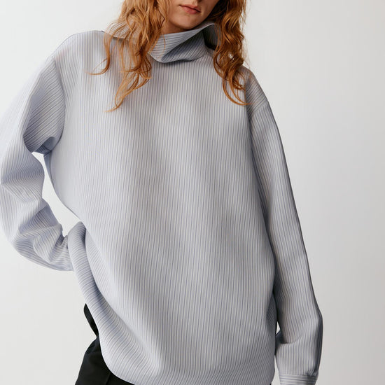 Video of a woman wearing a blue striped wool and silk blouse, showing the fluid movement of the relaxed silhouette and asymmetric hem as she moves.
