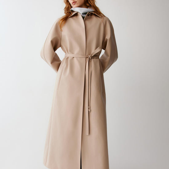 Video of a woman wearing a beige wool and silk trench coat, showing the movement of the long silhouette and fluid drape as she walks.