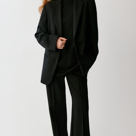 Video of a woman wearing a black wool blazer, showing the movement of the single-breasted silhouette and structured fabric as she moves.
