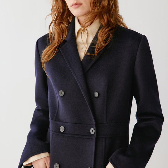 Video of a woman wearing a dark navy double-face wool coat, showing the long double-breasted silhouette and movement of the fabric as she moves.
