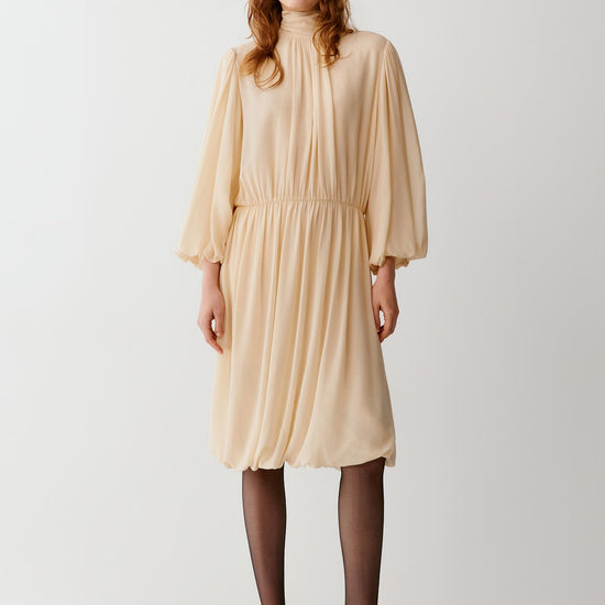 Video of a woman wearing an ivory silk georgette dress, showing the fluid movement of the gathered knee-length silhouette and voluminous sleeves as she moves.