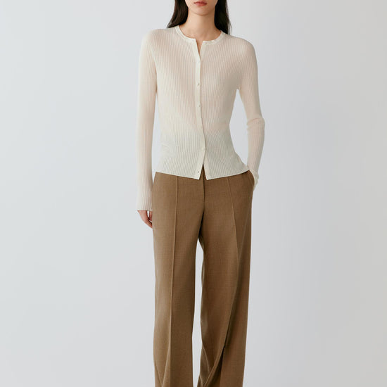 Video of a woman wearing a cream ribbed cardigan in worsted wool, showing the fitted silhouette, vertical ribbed texture and natural movement of the lightweight knit as she moves.